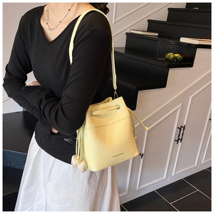 Close-up of yellow bucket bag with lychee texture and heart charm shown on model