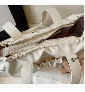 Detail view of large cream tote bag with cloud-like pleated edges and plush bear charm