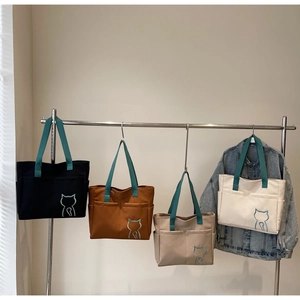 Detail of four colorful canvas tote bags with cat embroidery hanging on a metal rack