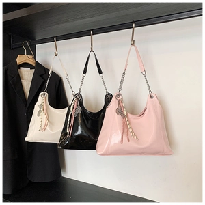 Three glossy leather tote bags in cream, black and pink with metal chains and charms