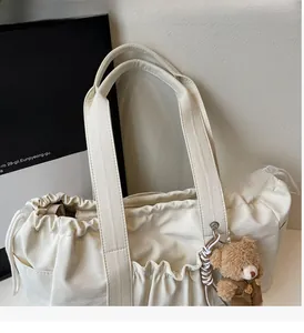 Detail of off-white canvas tote bag featuring drawstring closure and a plush bear pendant