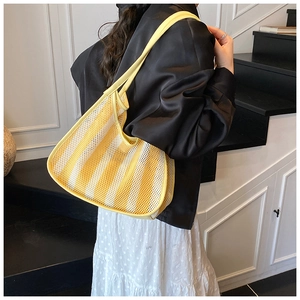 Detail of yellow and white striped mesh tote bag worn by model on a modern staircase