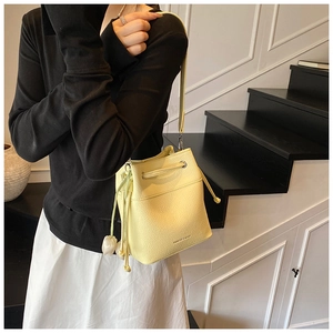 Detail of a creamy yellow drawstring bucket bag with lychee texture and thin strap