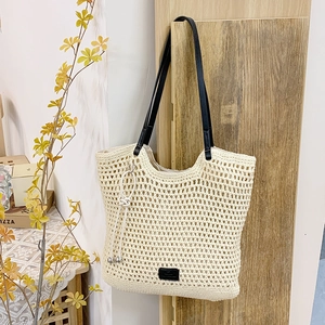 Detail of hollow crochet woven tote bag with faux leather straps and decorative knot tassel