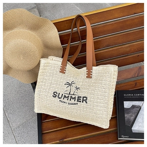 Detail of hand-woven straw tote bag with palm tree print and brown leather handles