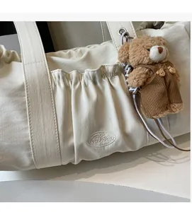 Detail of off-white tote bag featuring pleated front pocket and cute teddy bear charm