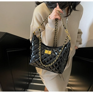 Detail of black patent leather quilted texture and gold square metal clasp on handbag