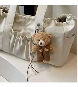 Detail of a creamy white drawstring tote bag with a cute brown teddy bear pendant