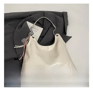 Detail of off-white leather hobo bag with metal chain and racket pendant on gray suit