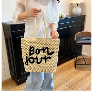 Détail du sac cabas tissé beige avec lettrage Bon jour brodé en noir et texture en paille
