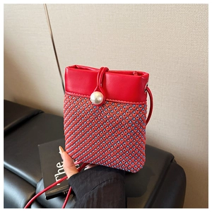 Detail showing the red and blue woven texture, pearl clasp, and red leather strap of the bag