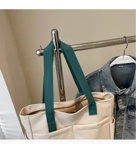 Detail view of large cream canvas tote with green straps and multi-pocket design