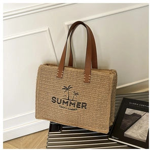 Detail of embroidered summer logo on large straw tote bag with brown leather handles