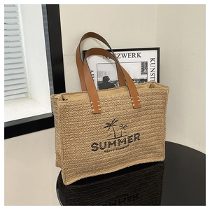 Detail of woven straw tote bag featuring black Summer embroidery and dark leather handles
