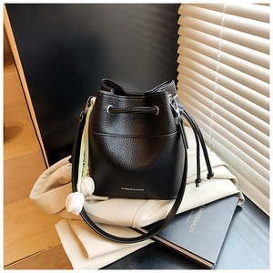 Close-up of black bucket bag with tulip charm and drawstring closure on beige blazer