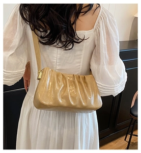 Detail of light brown cloud bag with pleats and gold metal buckle on a white dress