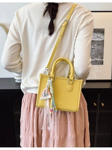 Chic yellow lychee leather handbag with rainbow charm shown in a stylish back-carry pose