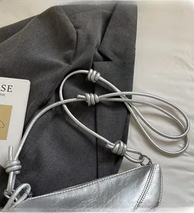 Detail of metallic silver crescent bag with decorative knotted shoulder straps on grey suit