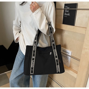 Detail of black tote bag featuring broad letter print shoulder strap and side pocket