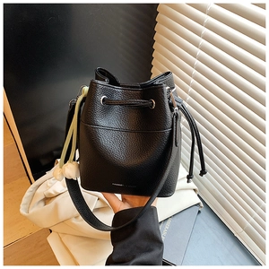Detail of black pebbled leather bucket bag with white floral charm and wide shoulder strap