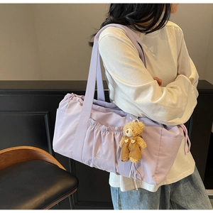 Detail of lavender nylon shoulder bag featuring side pockets and a plush bear charm