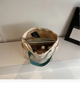 Top view of beige canvas tote with green straps showing large storage space and pockets