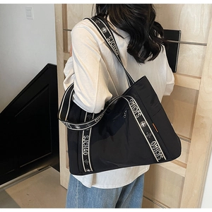 Detail of the black nylon tote bag showing the patterned shoulder strap and side orange accents