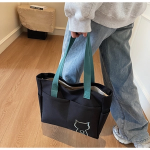 Close-up of black canvas tote bag with green handles and cute cat logo detail