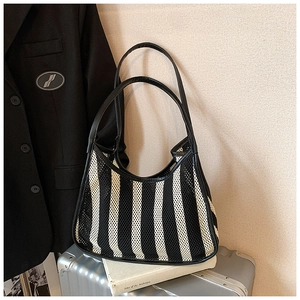 Chic striped mesh tote bag with black faux leather strap displayed on a travel suitcase