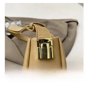 Detail of the golden push-lock hardware on a pleated khaki faux leather crossbody bag