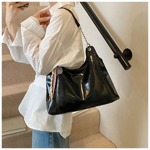 Detail of a large black patent leather tote bag with chain strap and scarf accessory