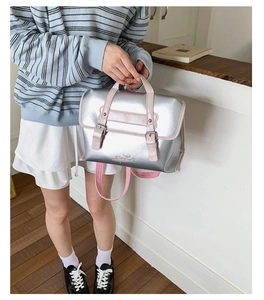 Detailed close-up of a silver metallic handbag with contrast pink top handles and logo