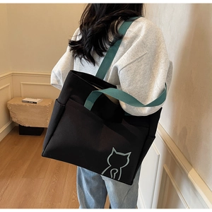Detail shot of a black canvas tote bag with green handles and cute cat logo on the side
