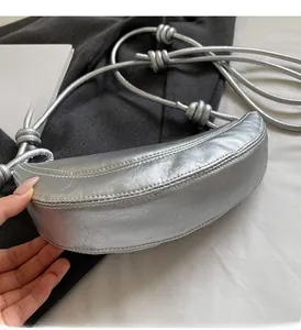 Detail of silver crescent bag featuring knotted shoulder strap and metallic leather texture