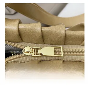 Close-up of a smooth gold metal zipper on a coffee-colored pleated cloud shoulder bag