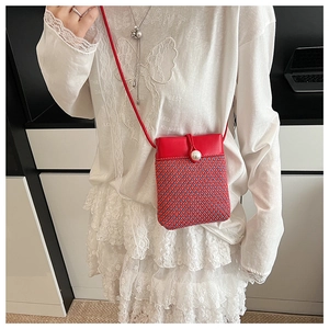 Detail of red and blue woven straw crossbody phone bag featuring a pearl clasp and red strap