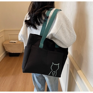 Detailed side view of black canvas tote bag featuring green strap and minimalist cat logo