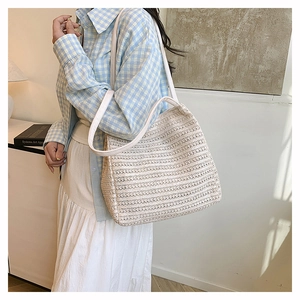 Detail of a woven tote bag featuring hollow texture and white leather straps worn by model