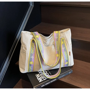 Detail of a large beige tote bag with a colorful woven shoulder strap and side pocket
