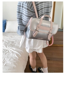 Modern silver mirror backpack with pink trim and top handle shown on a model in a bedroom