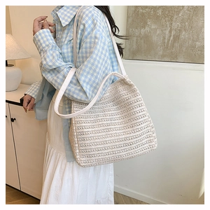 Detailed view of woven straw tote bag with white leather straps for summer style