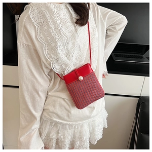 Detail of woven crossbody bag featuring red faux leather flap and large pearl closure