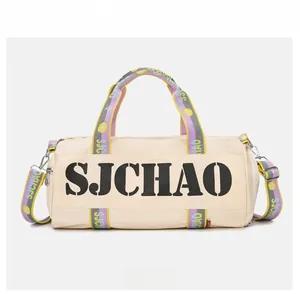Front view of white cylinder duffel bag with black lettering and colorful woven straps