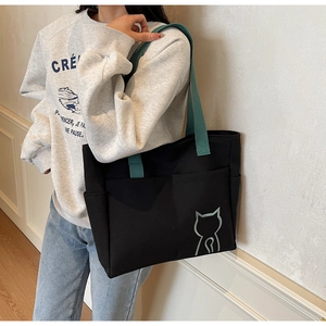 Detail of black canvas tote bag showing side pocket and minimalist green cat print