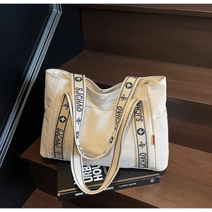 Detail of off-white tote bag showing woven shoulder strap and side storage pocket