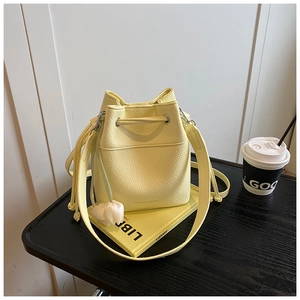 Pale yellow bucket bag with lychee texture and white tulip charm on a black desk