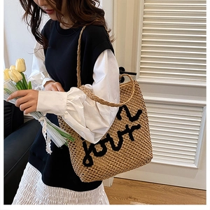 Détail du sac cabas en paille tissée avec broderie de lettres noires et anses