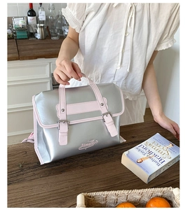 Detail of silver and pink handbag with dual retro buckle closure on a wooden table