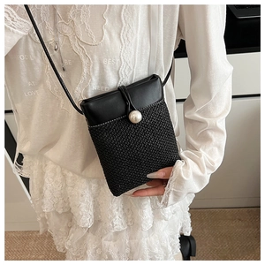 Detail of woven straw and black leather crossbody bag featuring a large pearl closure