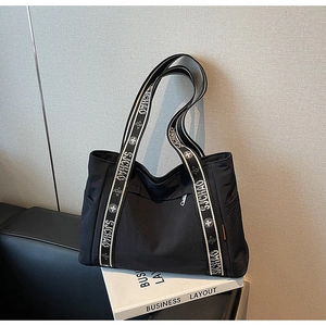 Detail of black tote bag featuring decorative SJCHAO printed wide canvas strap and zip closure